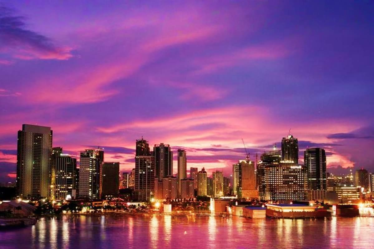 Best of Manila and Boracay Holiday Package City skyline of Manila at sunset with illuminated skyscrapers reflecting in water at dusk