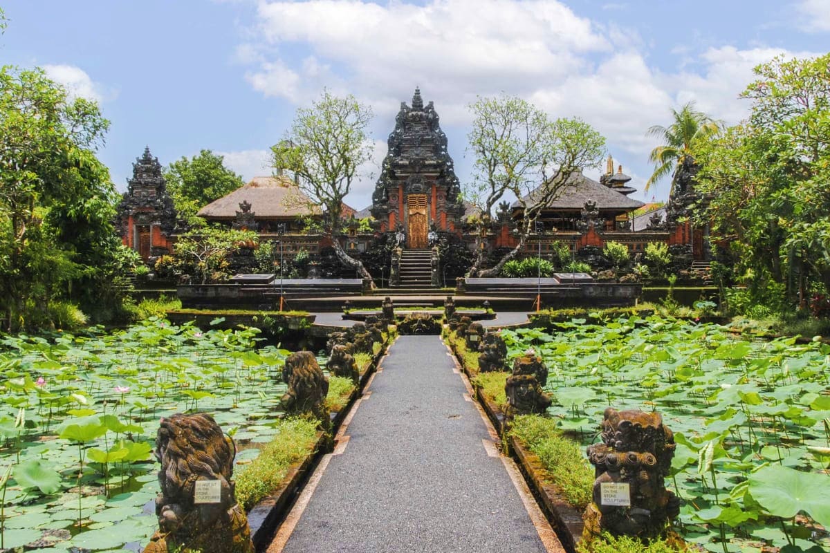 Balinese Hindu temple with ornate stone architecture surrounded by lily pond and lush tropical vegetation, with symmetrical p