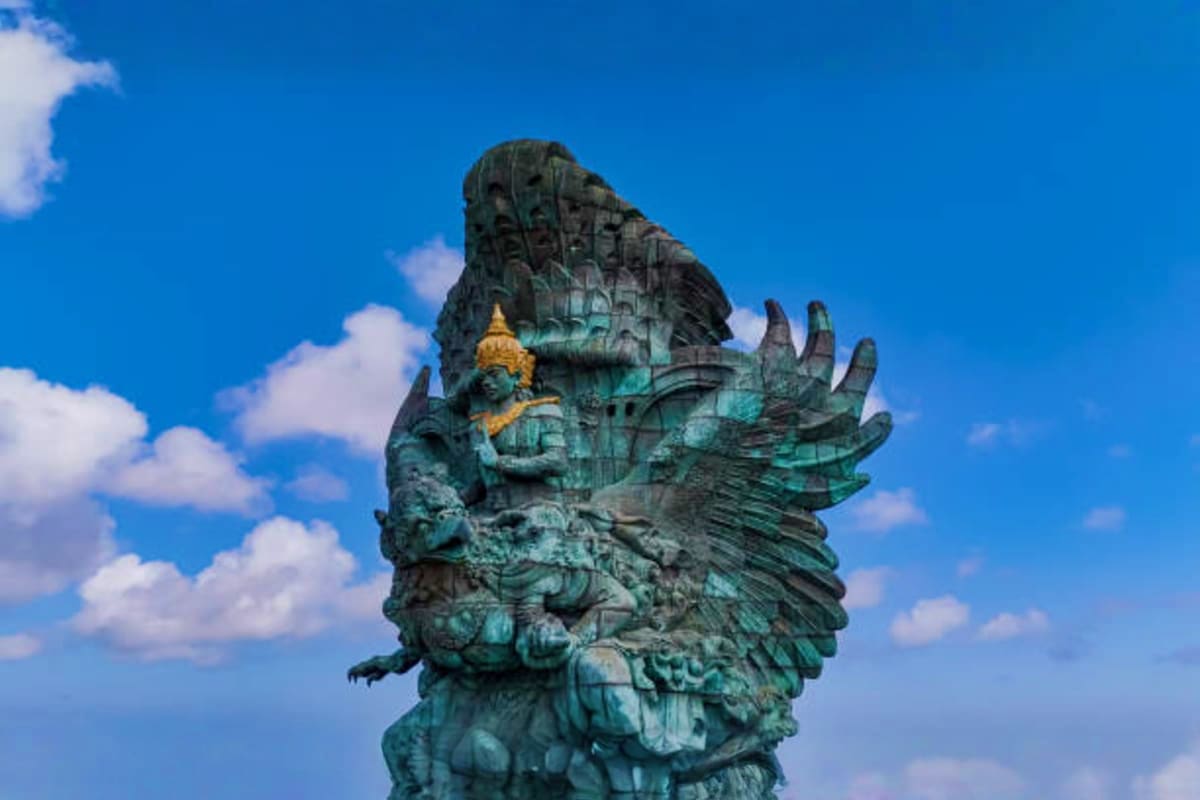 Giant winged stone statue with patina under blue sky and white clouds in Bali, Indonesia