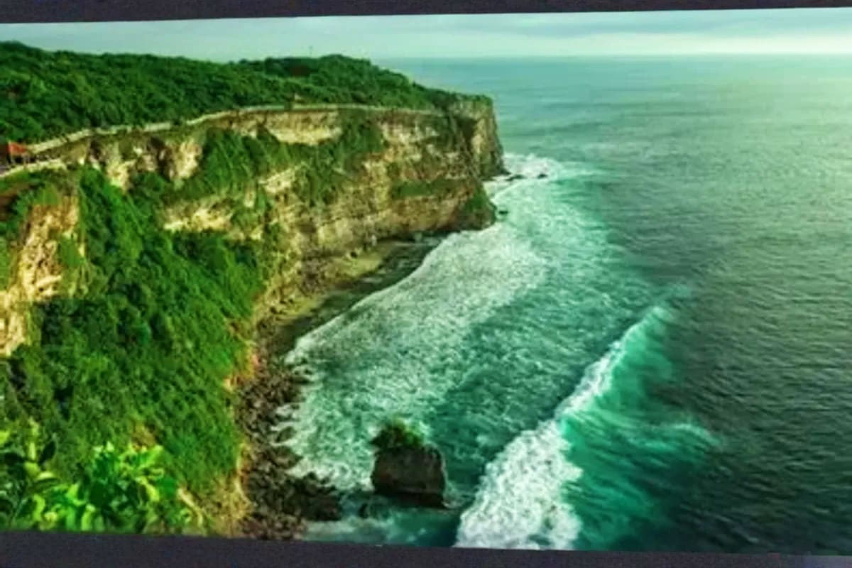 Dramatic coastal cliffs with lush green vegetation overlooking turquoise ocean waves crashing against rocky shoreline in Bali