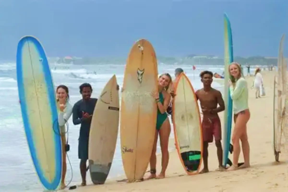 Group of diverse surfers holding surfboards on sandy beach with ocean waves in background