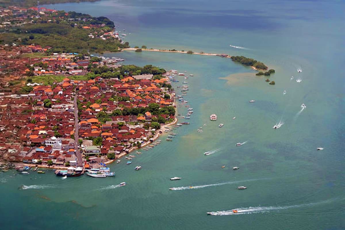 Aerial view of a densely populated coastal village in Bali with orange-roofed houses, fishing boats, and turquoise waters alo