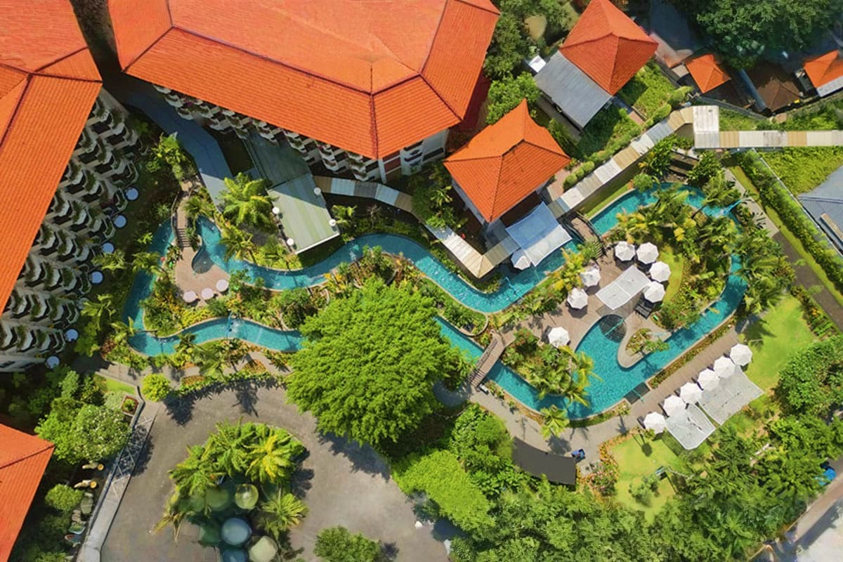 Aerial view of tropical resort with orange tile roofs, curved swimming pools, white umbrellas, and lush green landscaping