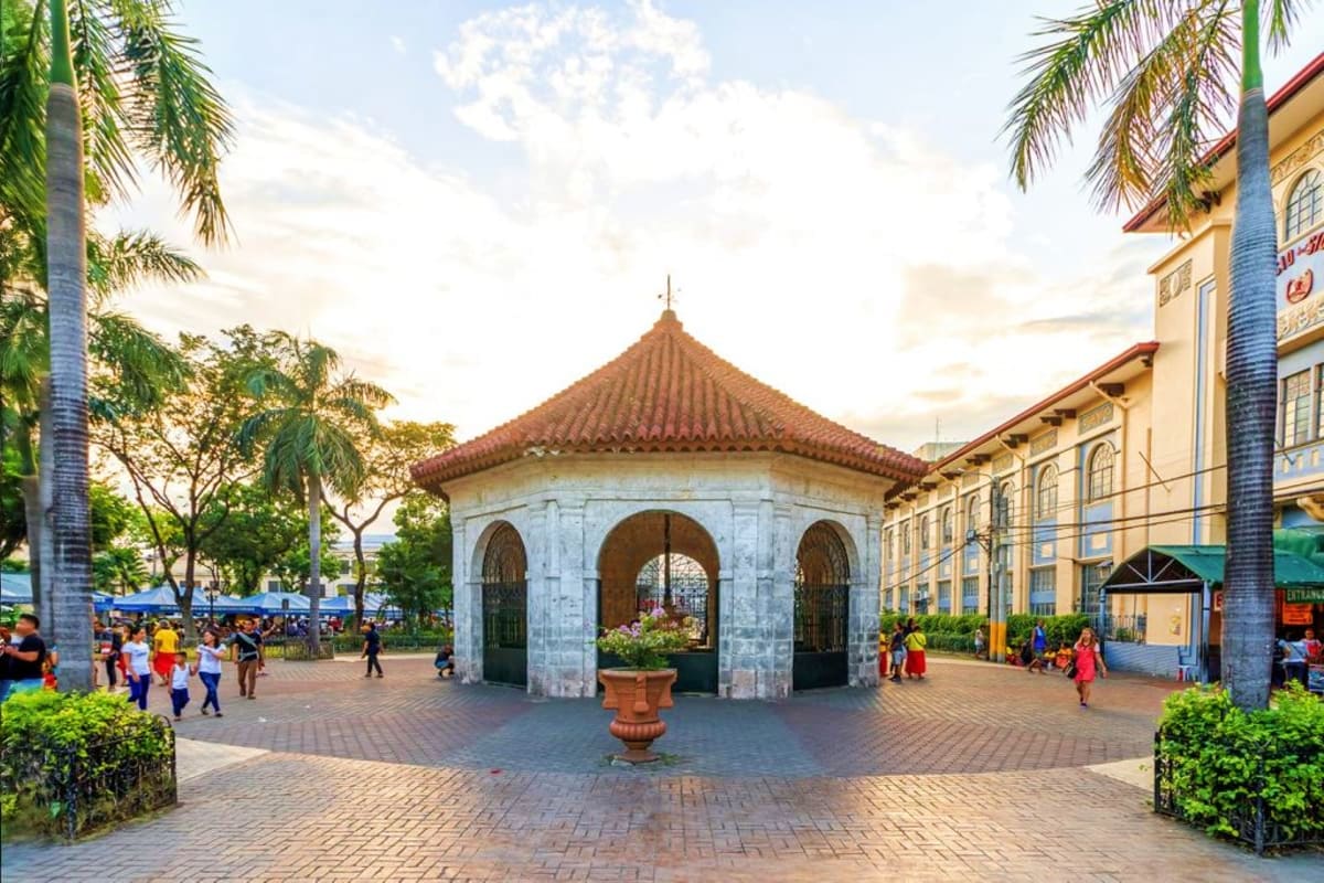6 Days Manila and Cebu Holiday Package Historic white octagonal gazebo with red-tiled roof in tropical plaza surrounded by palm trees and colonial buildings