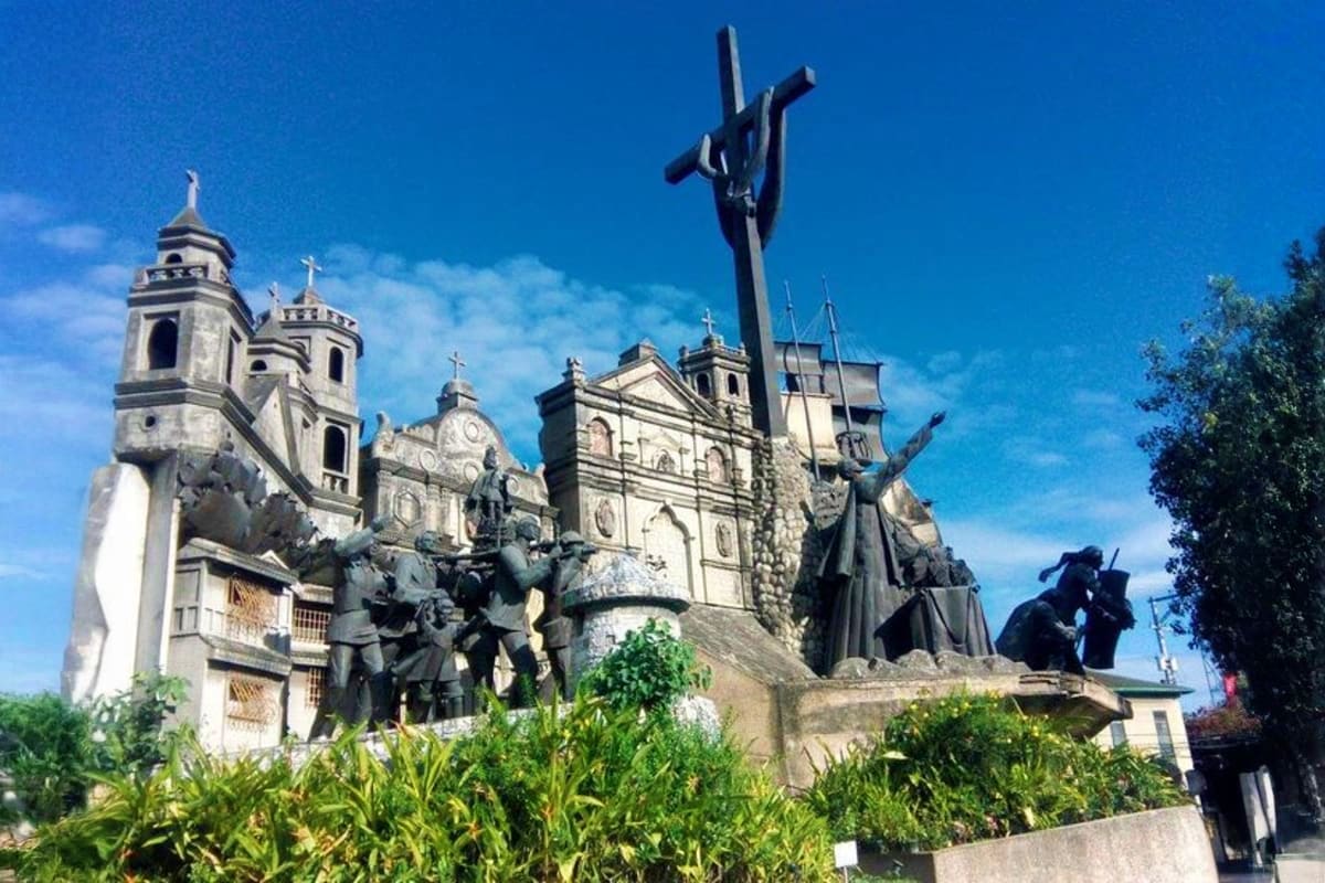 6 Days Manila and Cebu Holiday Package Historic stone monument with crosses and bronze sculptures in front of colonial church with bell towers under blue sky