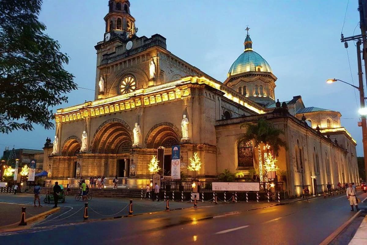 Best of Manila and Boracay Tour Package Illuminated historic church with golden dome and clock tower in downtown Manila at dusk, with pedestrians and decorated holid