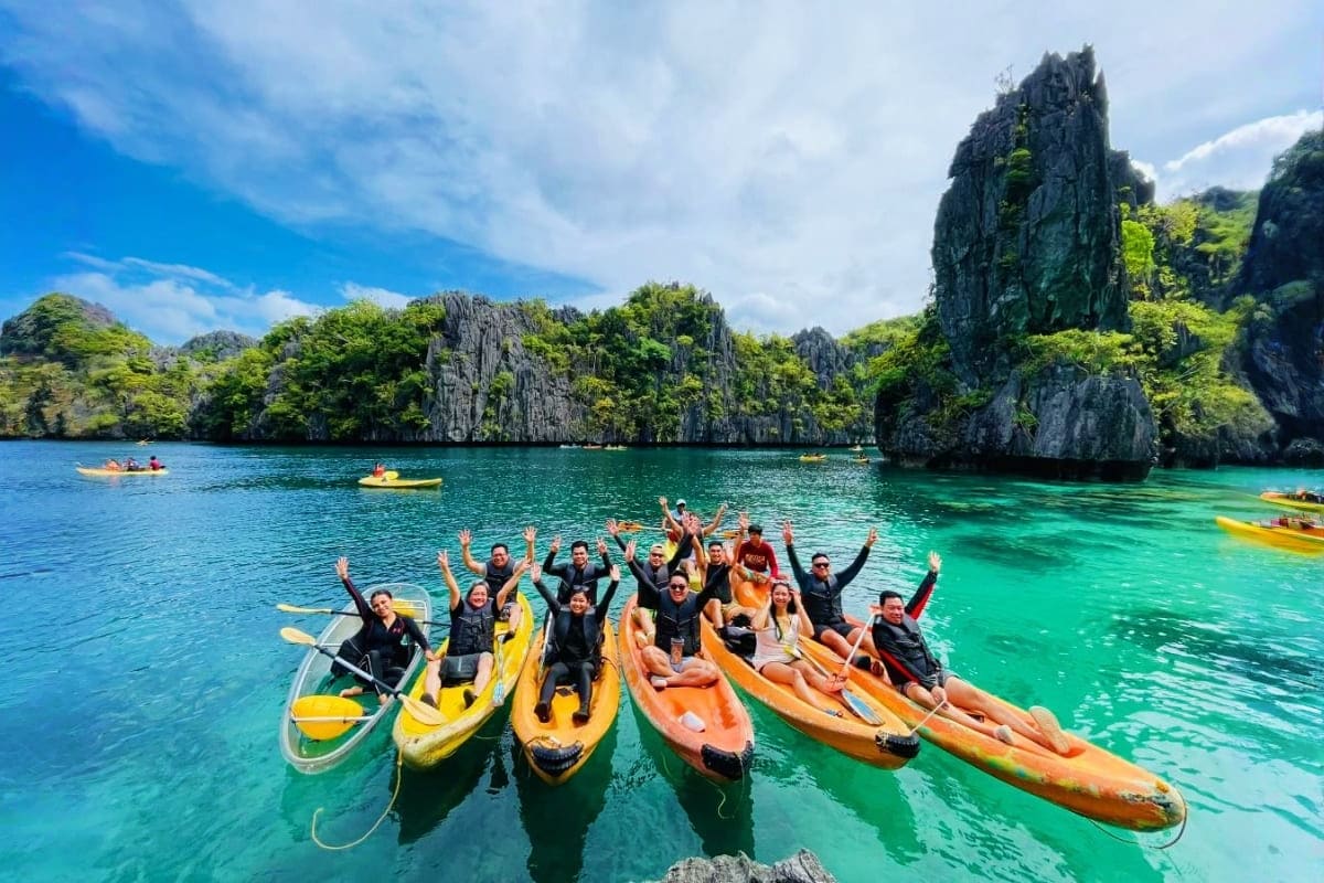 Philippines Island Escape with Manila El Nido and Cebu Group of tourists in colorful kayaks with raised arms in turquoise lagoon surrounded by tall limestone cliffs in El Nido, Phi