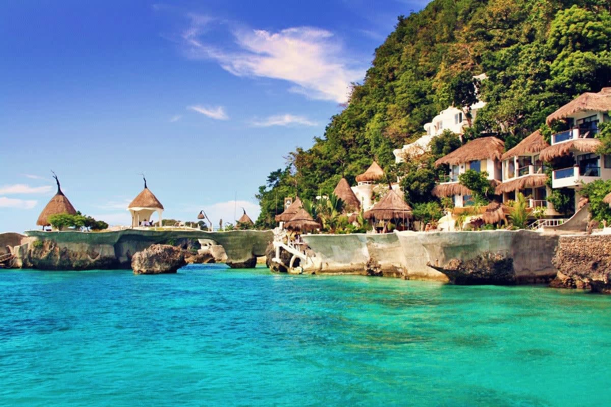 Tropical Philippines Vacation Tropical resort with thatched-roof bungalows and white buildings on rocky cliffs overlooking turquoise ocean waters in the Ph