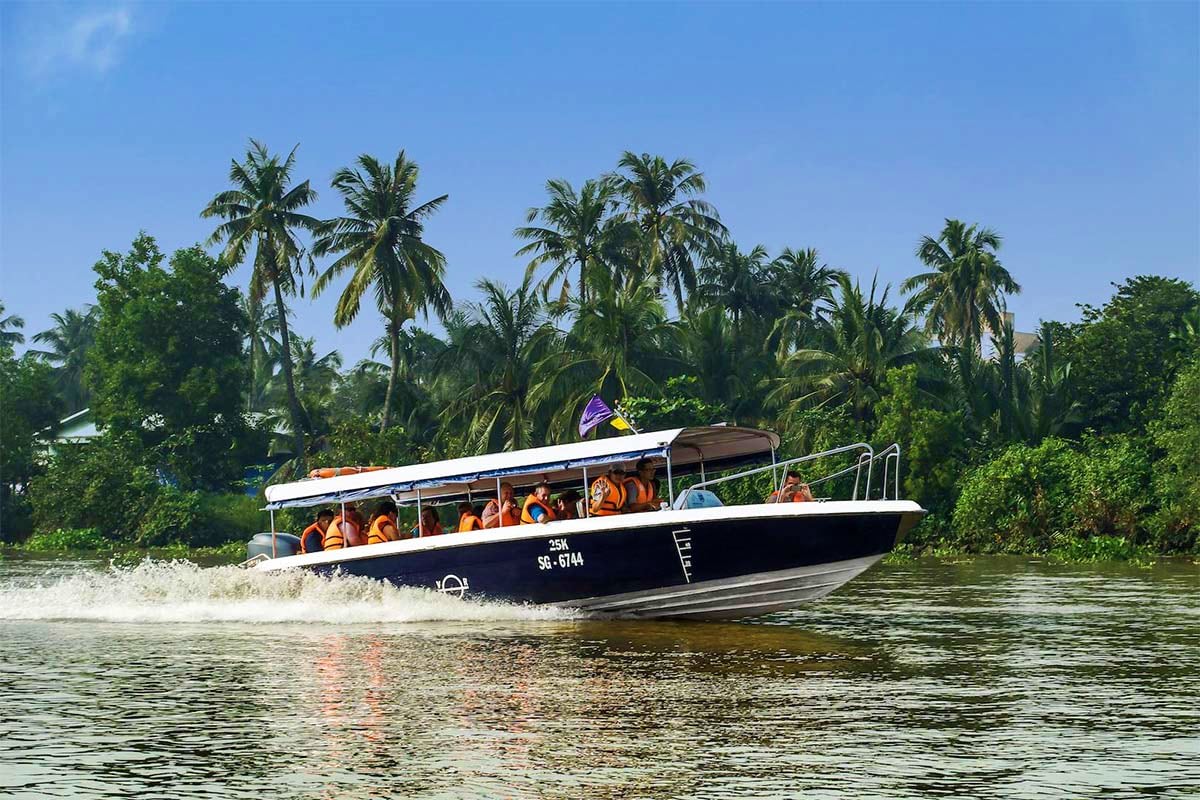 Speedboat with passengers wearing life jackets cruising through tropical waters with palm trees and lush vegetation in backgr