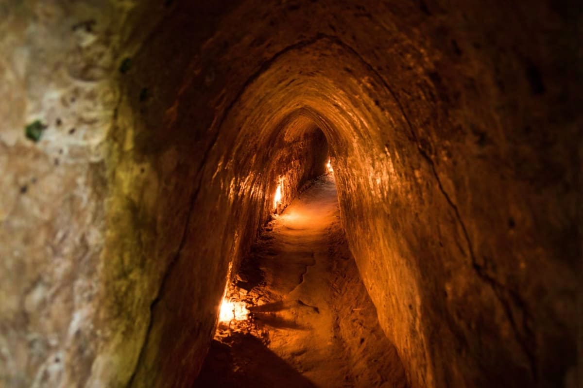 Illuminated underground tunnel with arched ceiling and warm golden lighting, showing historic cave passage with textured rock