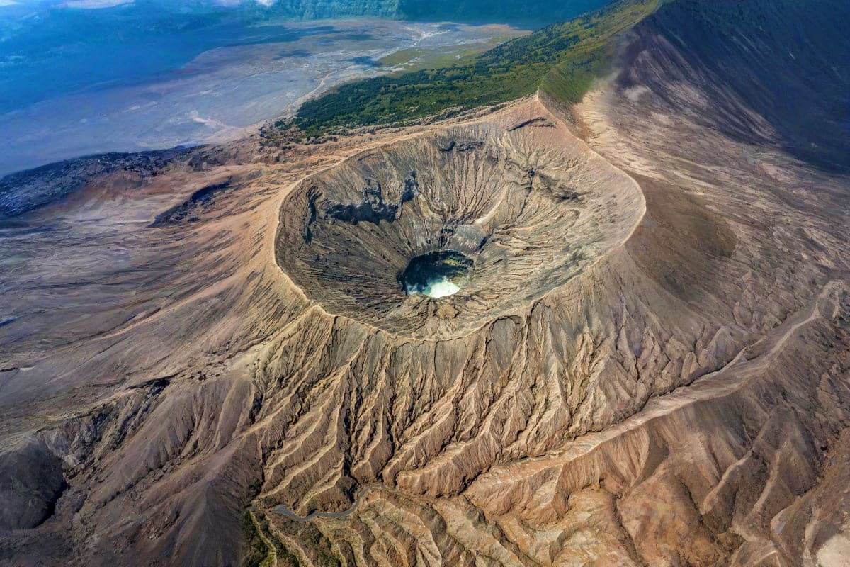 Aerial view of active volcano crater with crater lake, surrounded by barren volcanic slopes and forested ridges in Azerbaijan