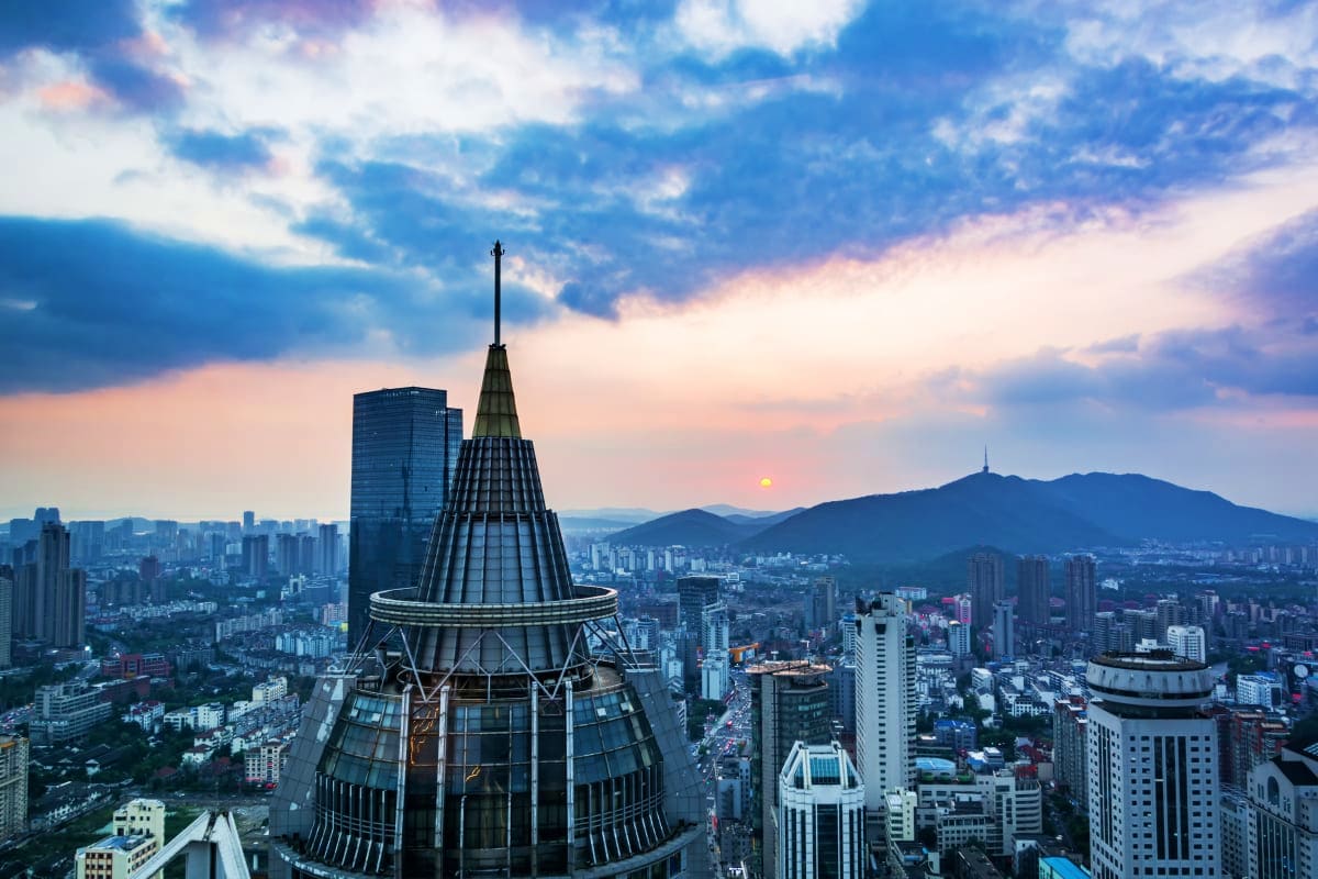 Aerial view of Baku cityscape at sunset with modern skyscrapers, distinctive cone-shaped tower, and mountains in the distance
