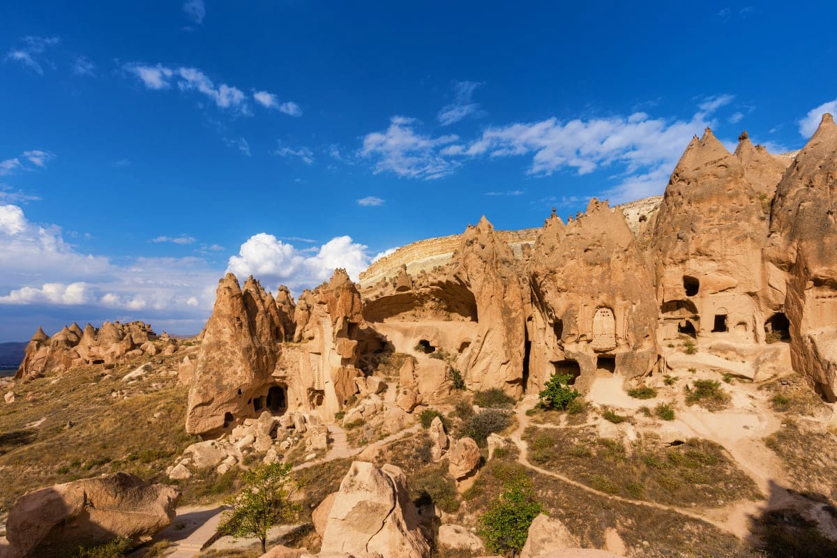 Ancient carved cave dwellings in Cappadocia with distinctive fairy chimneys and rock formations under blue sky