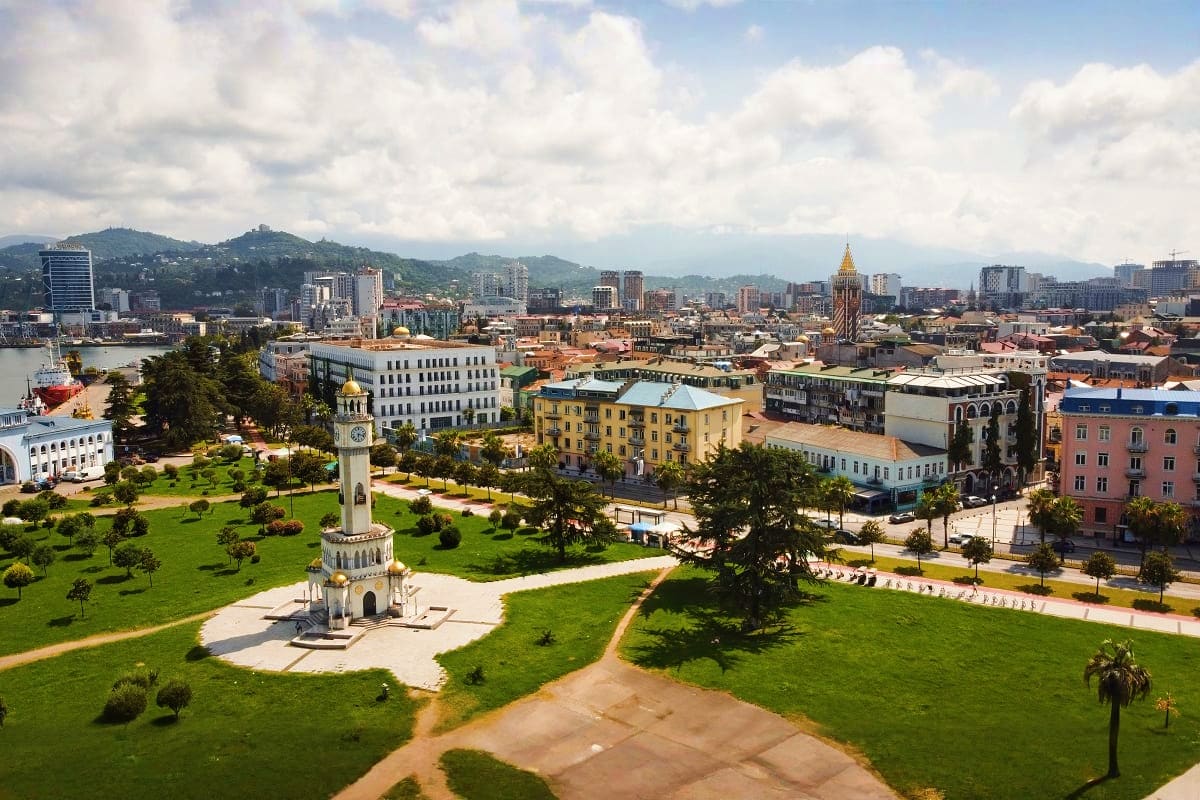 Aerial view of Tbilisi cityscape with Metekhi Church tower in foreground, surrounding mountains, and colorful historic buildi