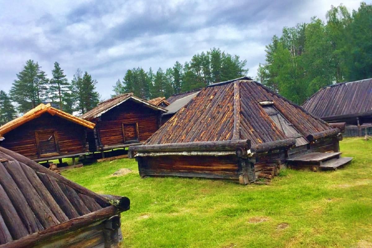 Traditional wooden log cabins with peaked roofs in a Nordic forest setting, representing authentic Russian countryside archit