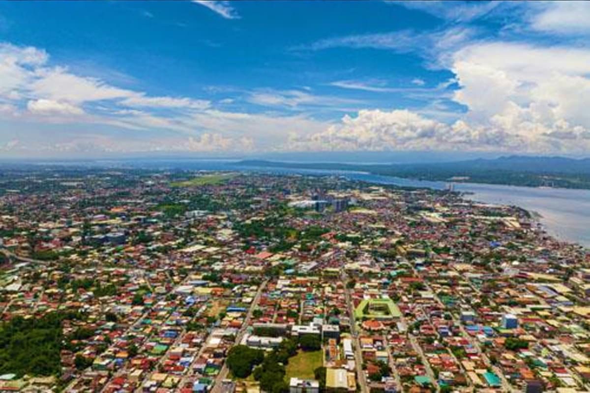Davao Siargao Wildlife Rafting Package Aerial view of Davao city with residential areas, waterfront, and mountains under blue sky with white clouds