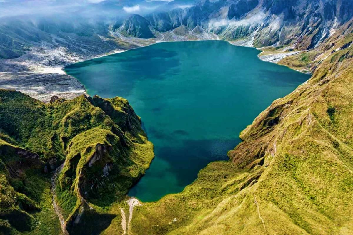 Manila Angeles Budget Tour Aerial view of a turquoise alpine lake surrounded by moss-covered mountains and rocky peaks in a scenic mountain valley