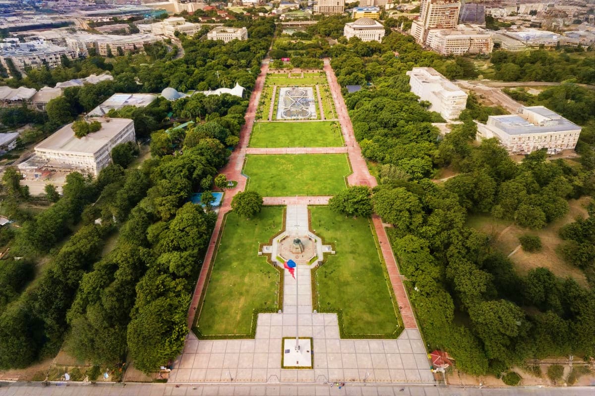 Manila Angeles Budget Tour Aerial view of a formal geometric garden with red brick pathways, green lawns, central monument with flag, surrounded by tree