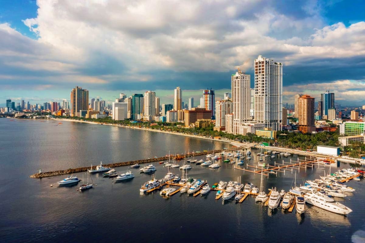 Manila Angeles Budget Tour Aerial view of Waikiki beachfront with high-rise hotels, marina with moored boats, and ocean under cloudy sky