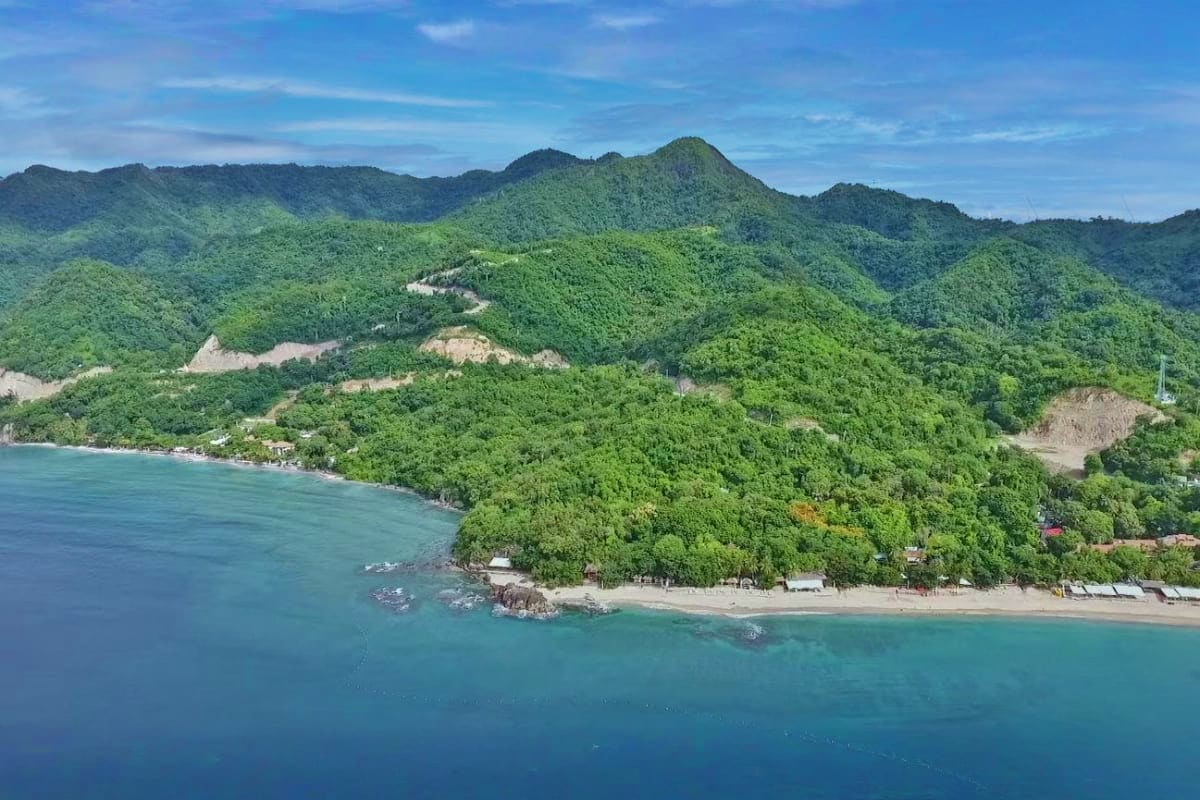 Manila Batangas Short Tour Aerial view of a tropical coastal landscape with lush green mountains, a winding river, sandy beach, and turquoise waters nea