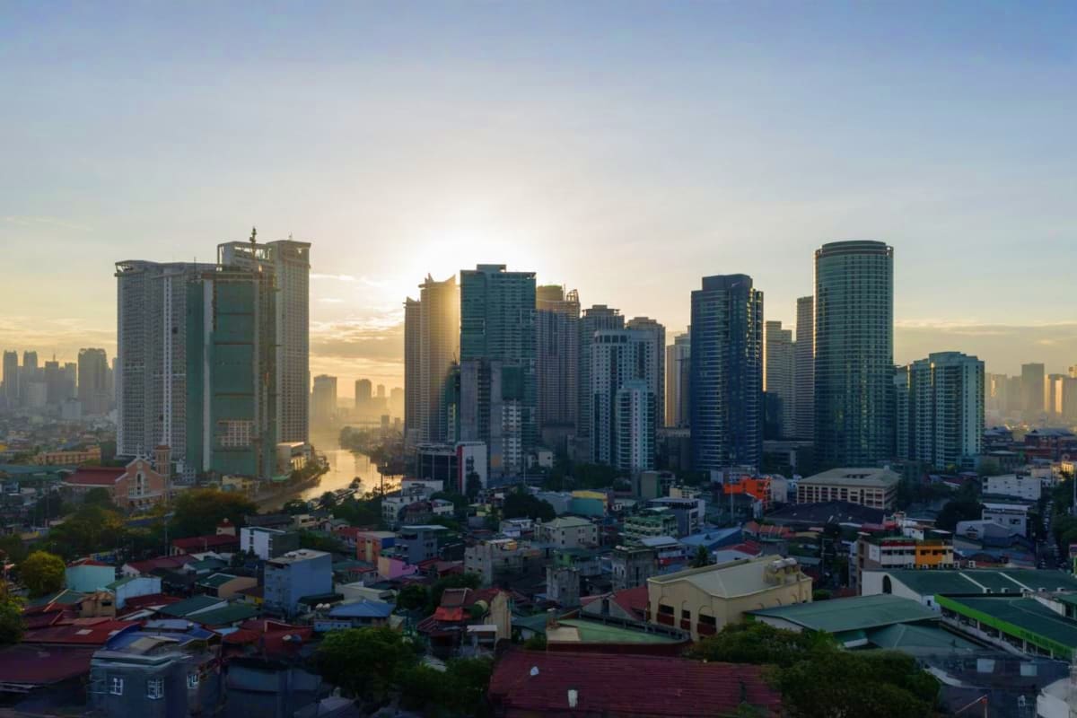 Manila Batangas Short Tour Manila cityscape at sunrise showing modern high-rise buildings and river with low-rise residential buildings in foreground