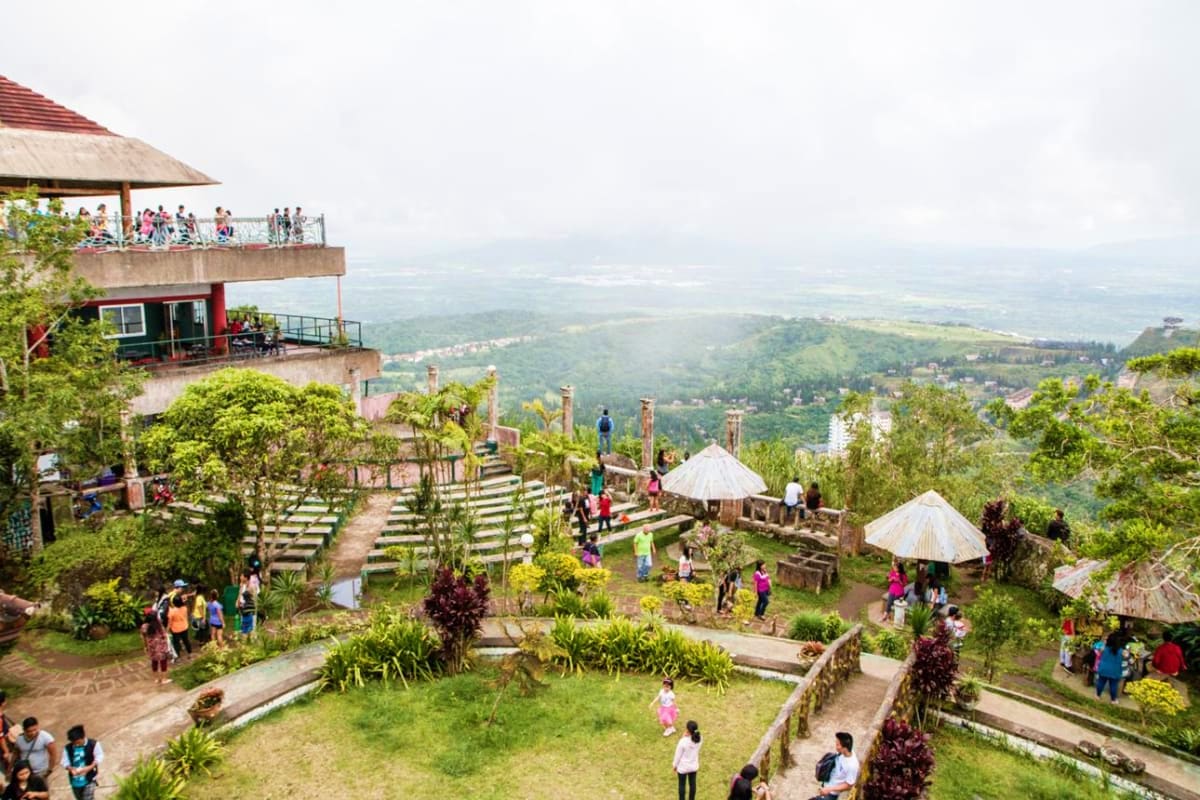 Manila Batangas Short Tour Tourists exploring a hillside garden resort with terraced walkways, white umbrellas, and expansive valley views in Batangas