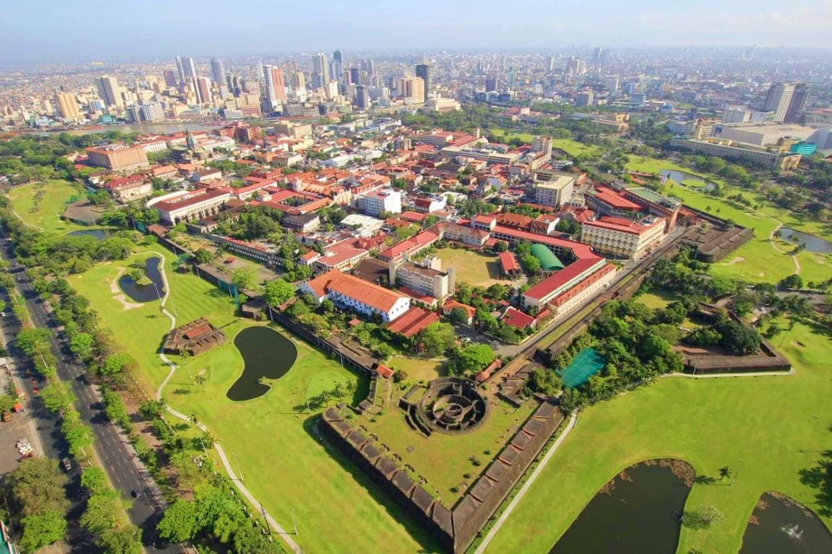 Exclusively Manila Aerial view of Intramuros historic walled city in Manila with red-roofed colonial buildings, green spaces, and modern skyline
