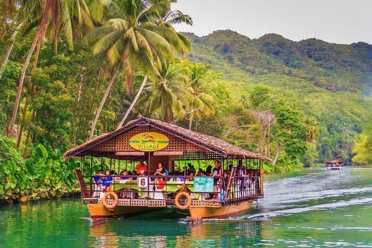 Simply Bohol Traditional wooden floating village restaurant on turquoise river surrounded by palm trees and lush green mountains in Bohol