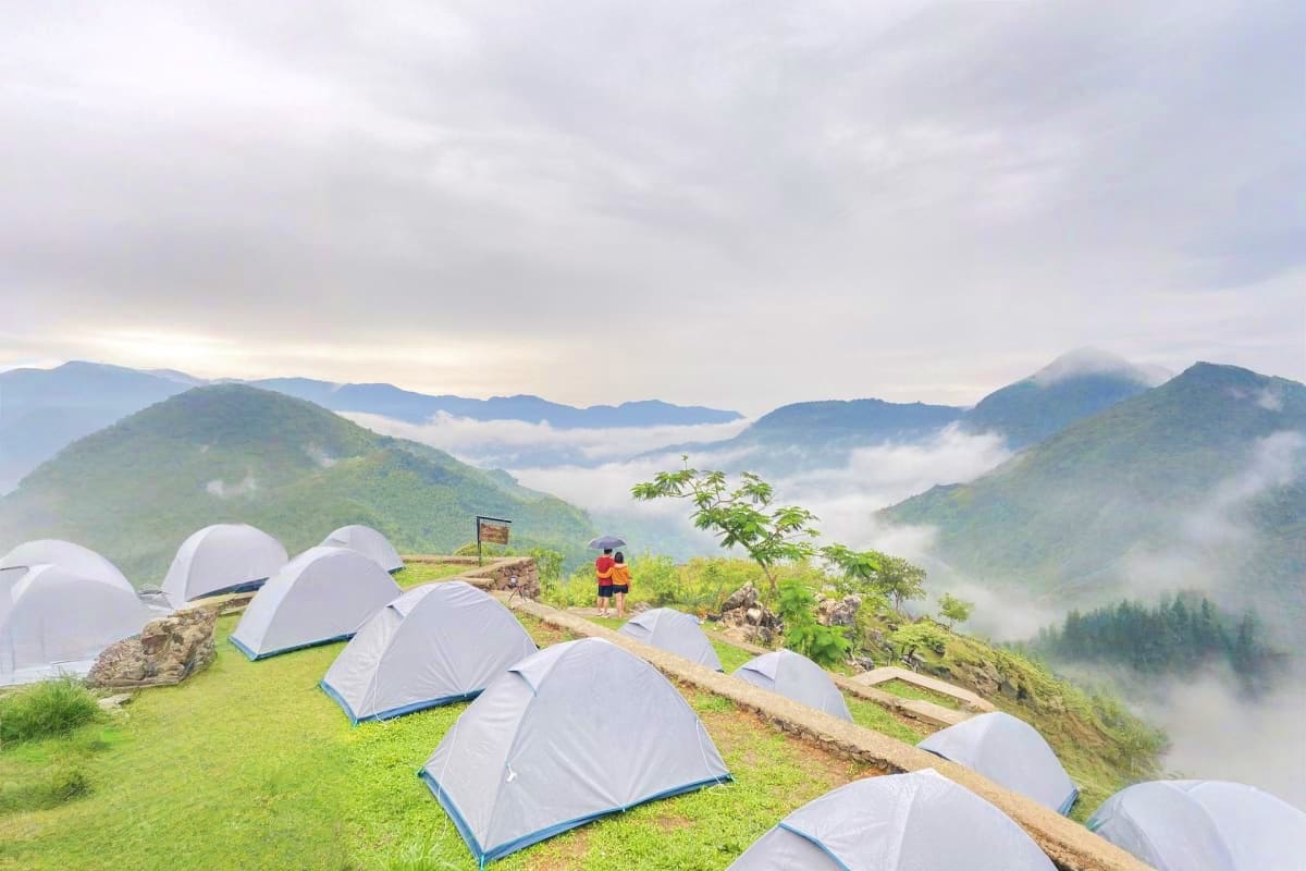Manila Glamping White dome tents pitched on a mountain meadow overlooking misty valleys and forested peaks at a glamping campsite.