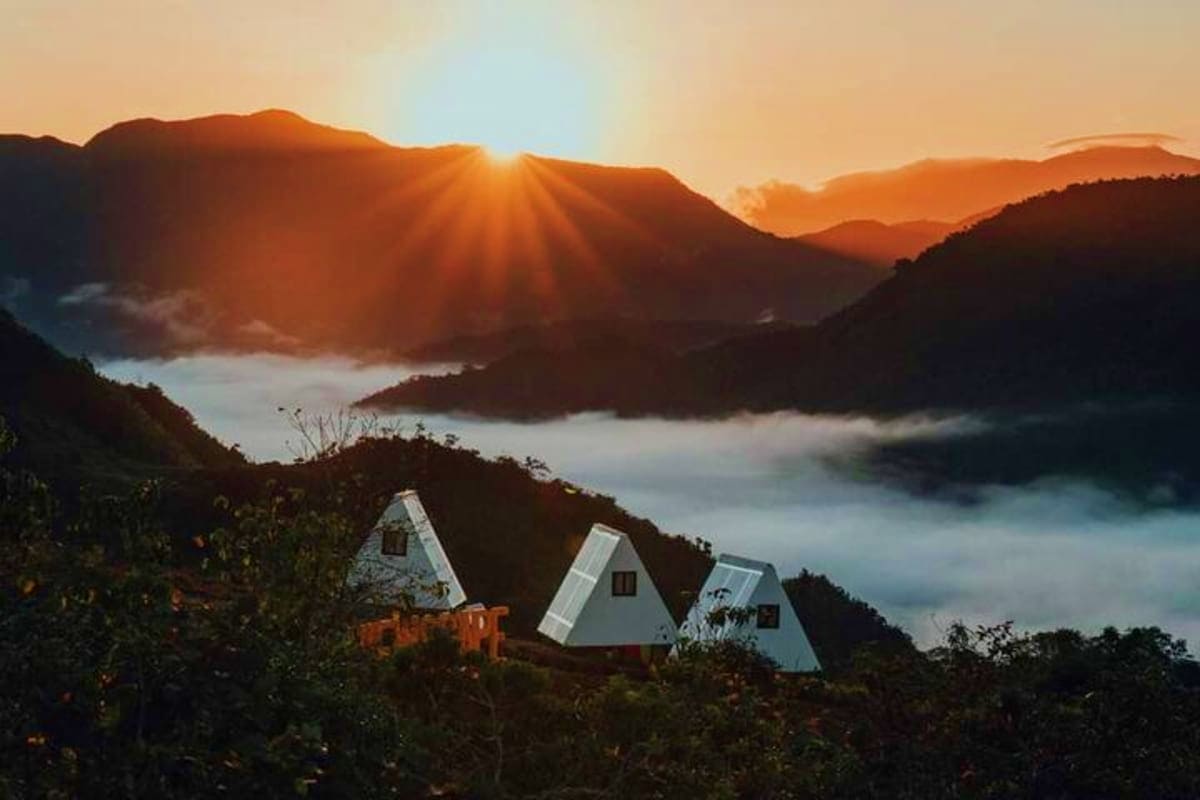Manila Glamping White A-frame glamping cabins on a misty mountainside at sunrise with valley and forested peaks below
