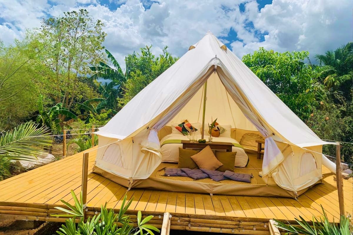 Manila Glamping Luxury bell tent glamping setup on wooden deck surrounded by tropical vegetation and blue sky with clouds