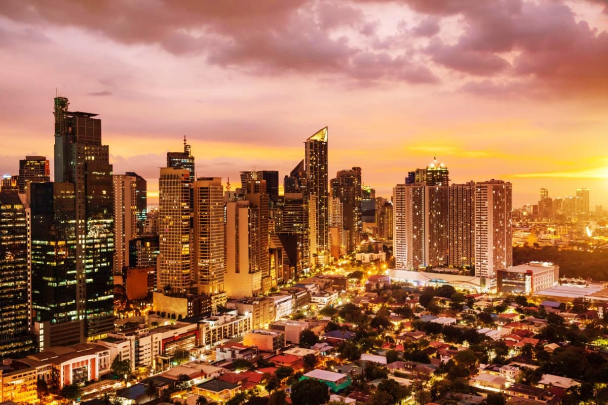 Manila Glamping Manila skyline at sunset with illuminated skyscrapers and low-rise buildings below during golden hour