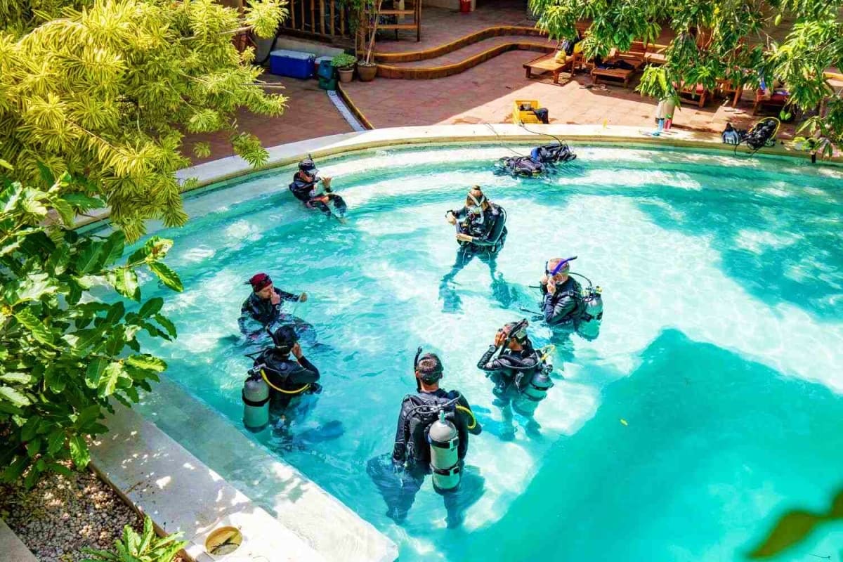 Puerto Galera Diving Tour Group of scuba divers in full gear training in a turquoise pool surrounded by tropical plants and resort facilities