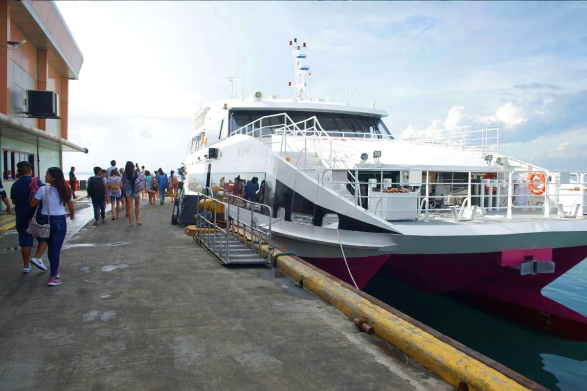 Island Escape Package Passengers boarding a white and burgundy ferry vessel at a concrete pier, with metal gangway and navigation equipment visible