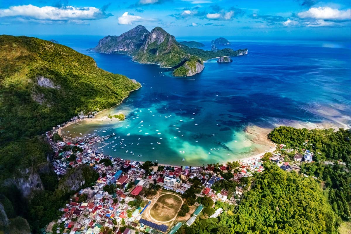 El Nido Escape Tour Aerial view of El Nido bay with limestone cliffs, turquoise waters, boats, and coastal town nestled between jungle and sea