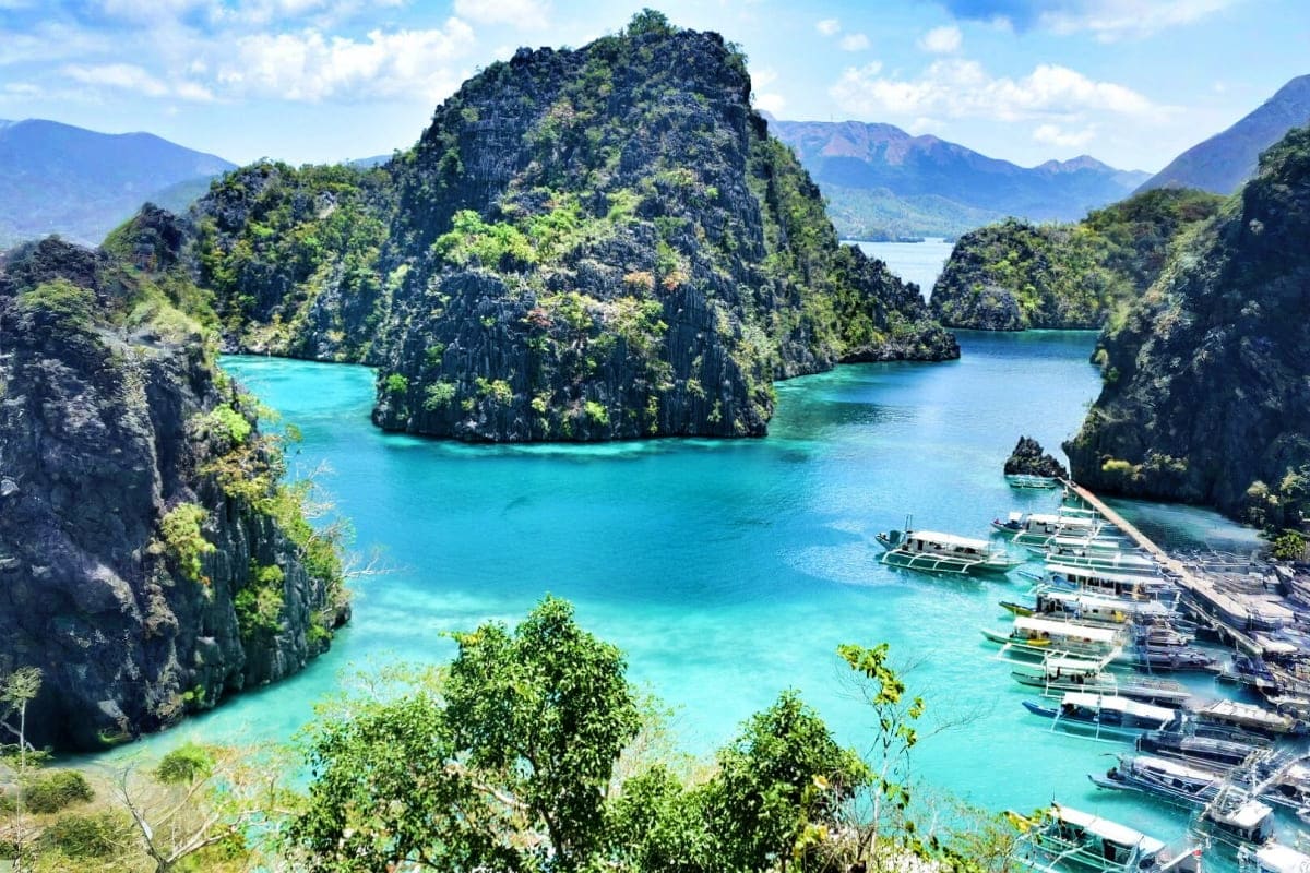 Manila Coron Escape Tour Tropical lagoon with turquoise water surrounded by limestone cliffs covered in green vegetation and traditional Filipino boat