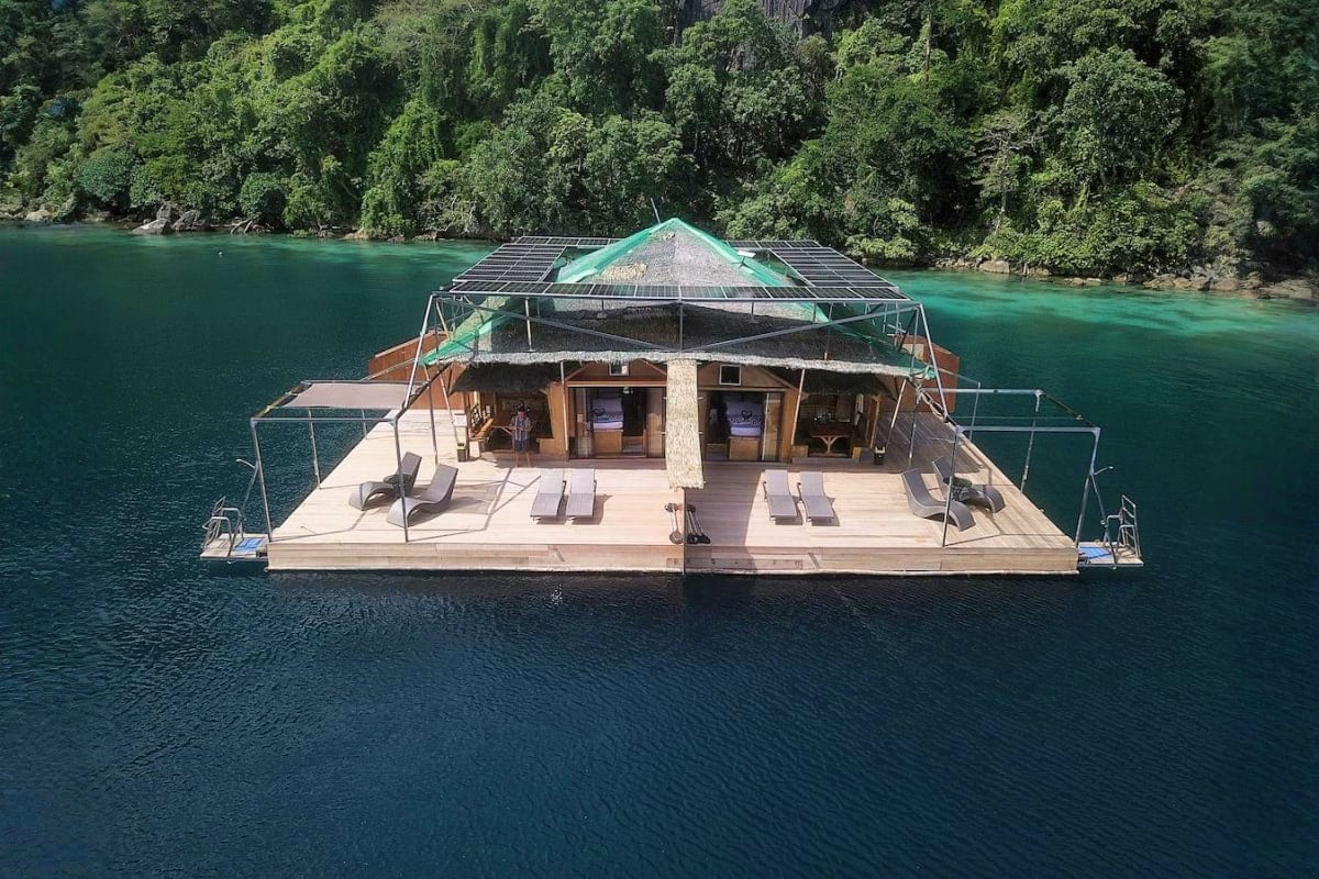 Manila Coron Escape Tour Luxury houseboat floating on turquoise water surrounded by dense green forest, featuring open-air deck with lounge chairs and