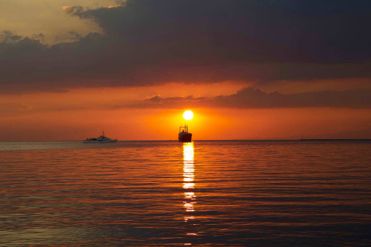 Manila Coron Escape Tour Ships silhouetted against golden sunset over calm ocean waters with sun reflecting on sea surface