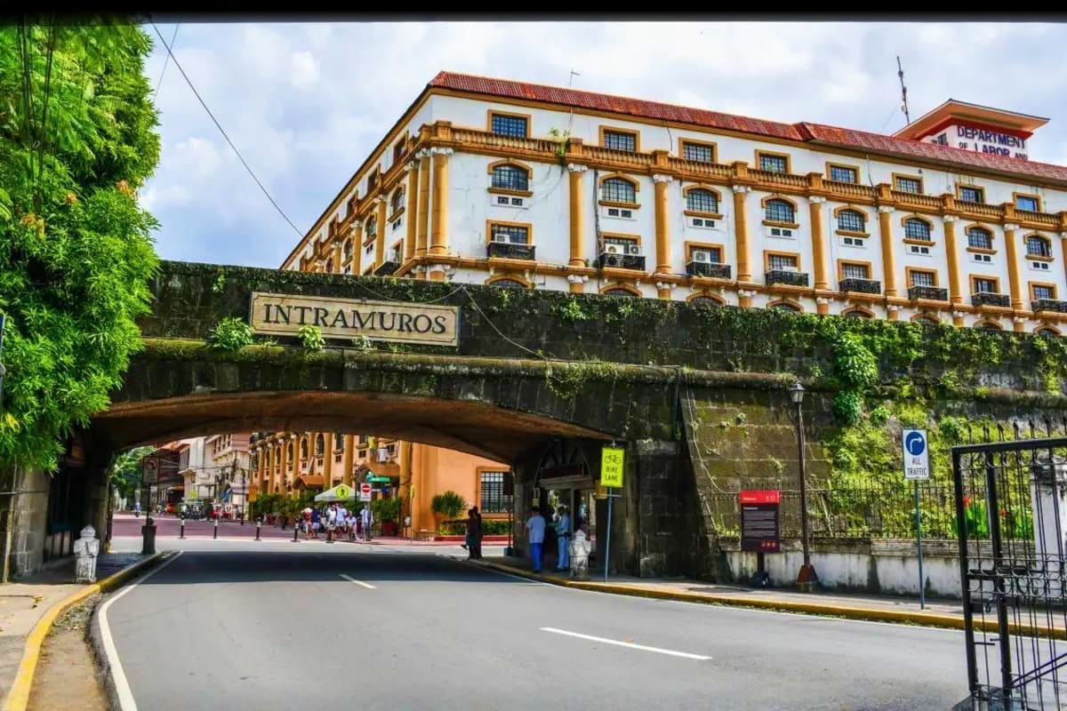 Pristine Palawan Tour Historic colonial building with yellow columns and "Intramuros" sign above stone archway bridge in Manila, Philippines