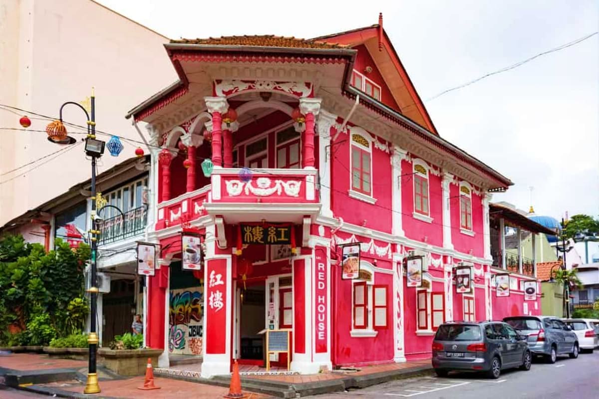 Bright red and white colonial-style building with Chinese architectural details and signage in a Malaysian street setting