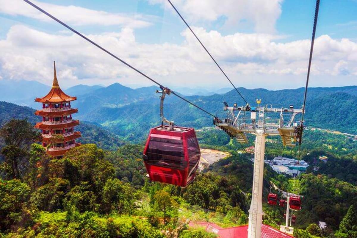 Red cable car ascending over forested mountains with traditional Asian pagoda temple visible in landscape below