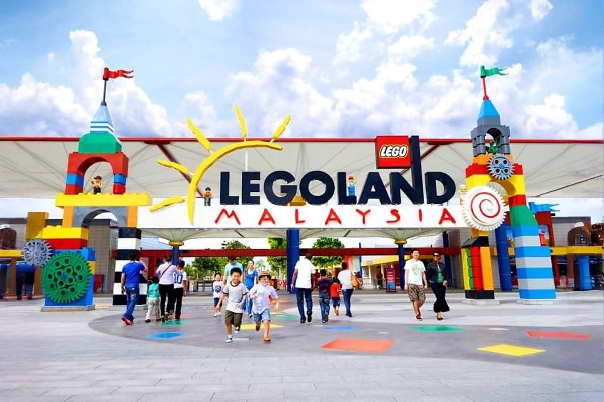 LEGOLAND Malaysia entrance with colorful brick structures, towers with flags, families walking through plaza, and blue sky wi