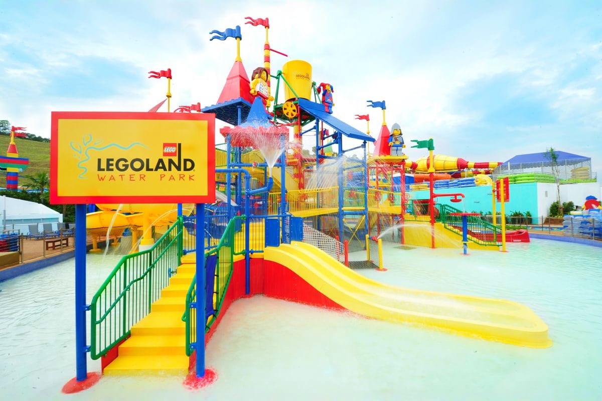 Colorful LEGOLAND Water Park attraction with bright yellow slide, red and blue castle tower, flags, and shallow water play ar