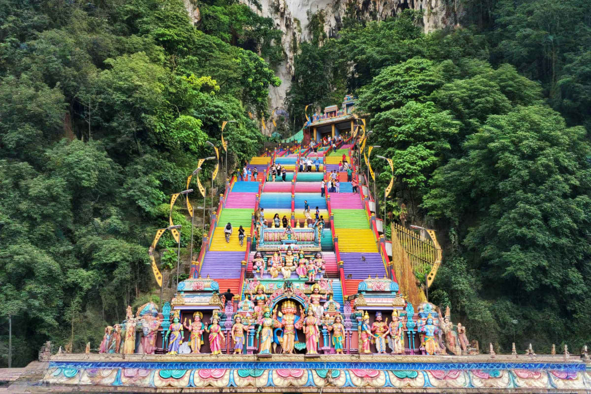 Colorful rainbow staircase at Batu Caves temple in Malaysia with ornate Hindu statues, limestone cliffs, and visitors climbin