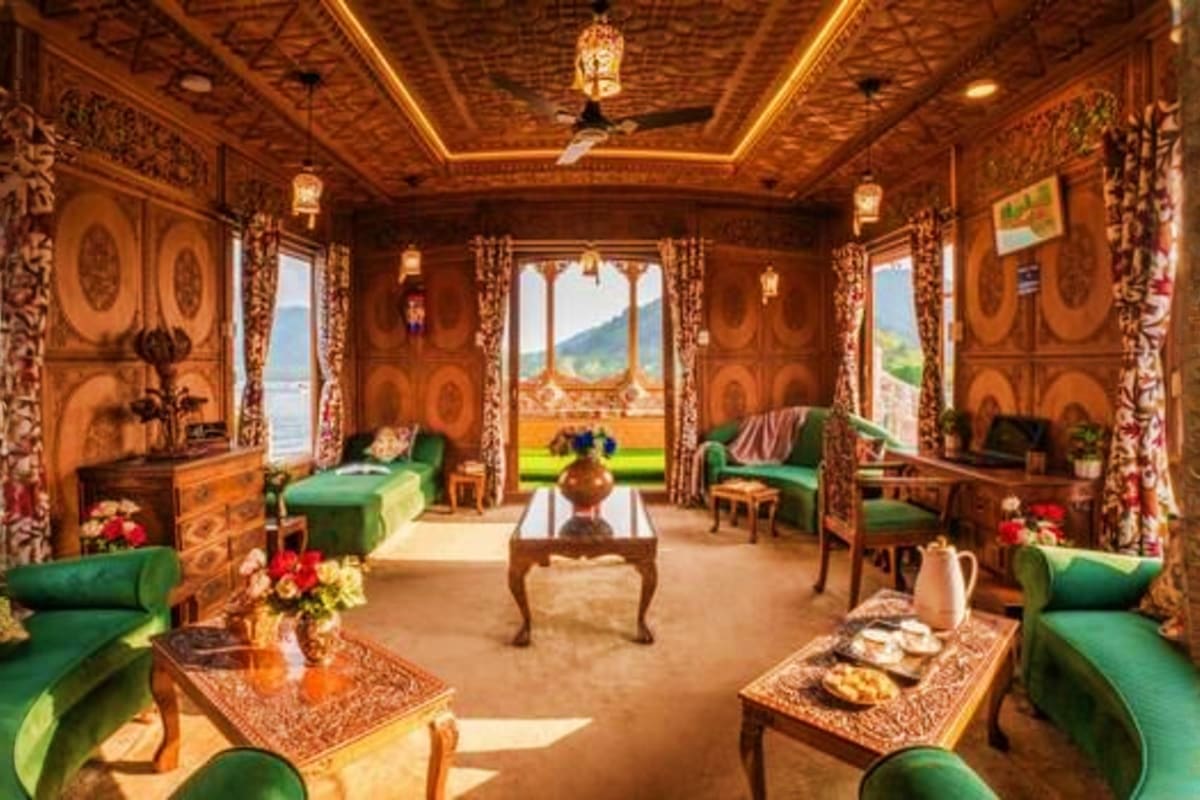 Luxury houseboat interior in Kashmir with ornate wooden carved panels, green velvet seating, and scenic lake and mountain vie