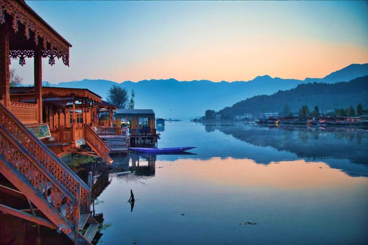 Traditional wooden houseboats with ornate carved railings on calm Dal Lake at sunrise, snow-capped mountains in background, K