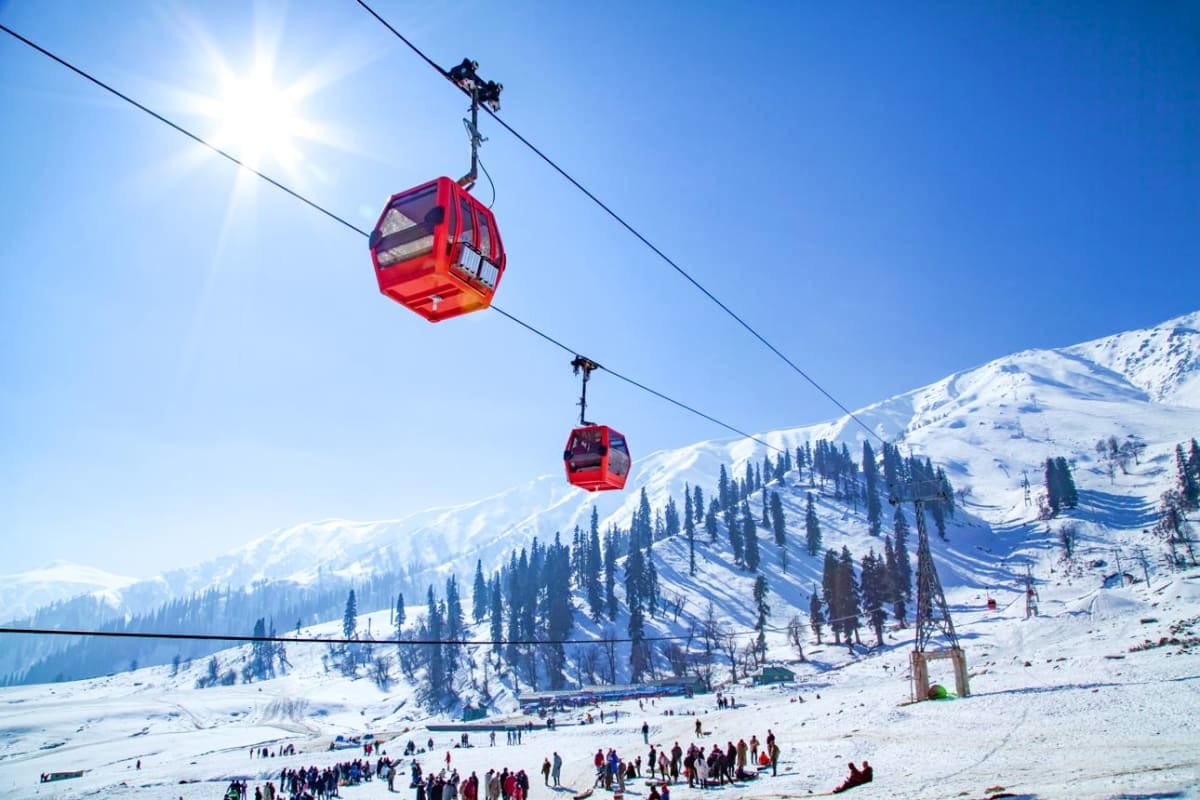 Red cable car gondolas suspended over snow-covered mountain with pine trees and tourists below in winter landscape
