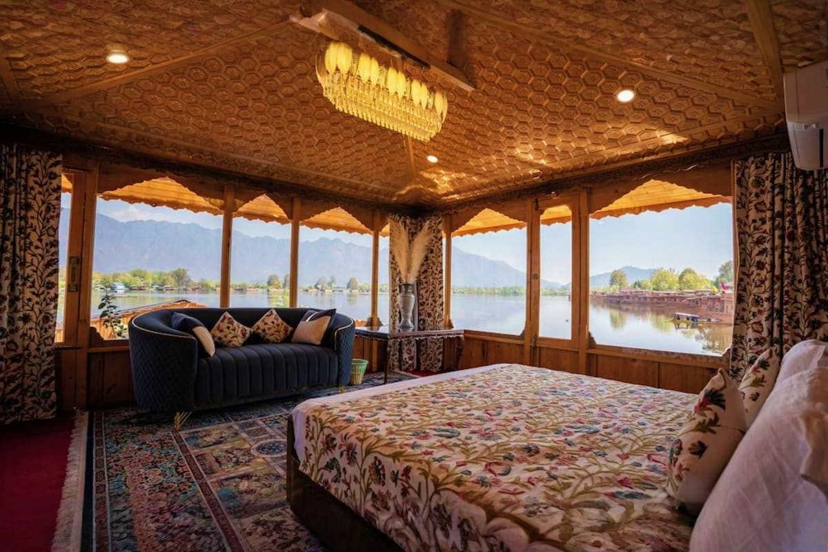 Luxury houseboat bedroom with panoramic windows overlooking Dal Lake and mountains in Kashmir, featuring ornate ceiling and t
