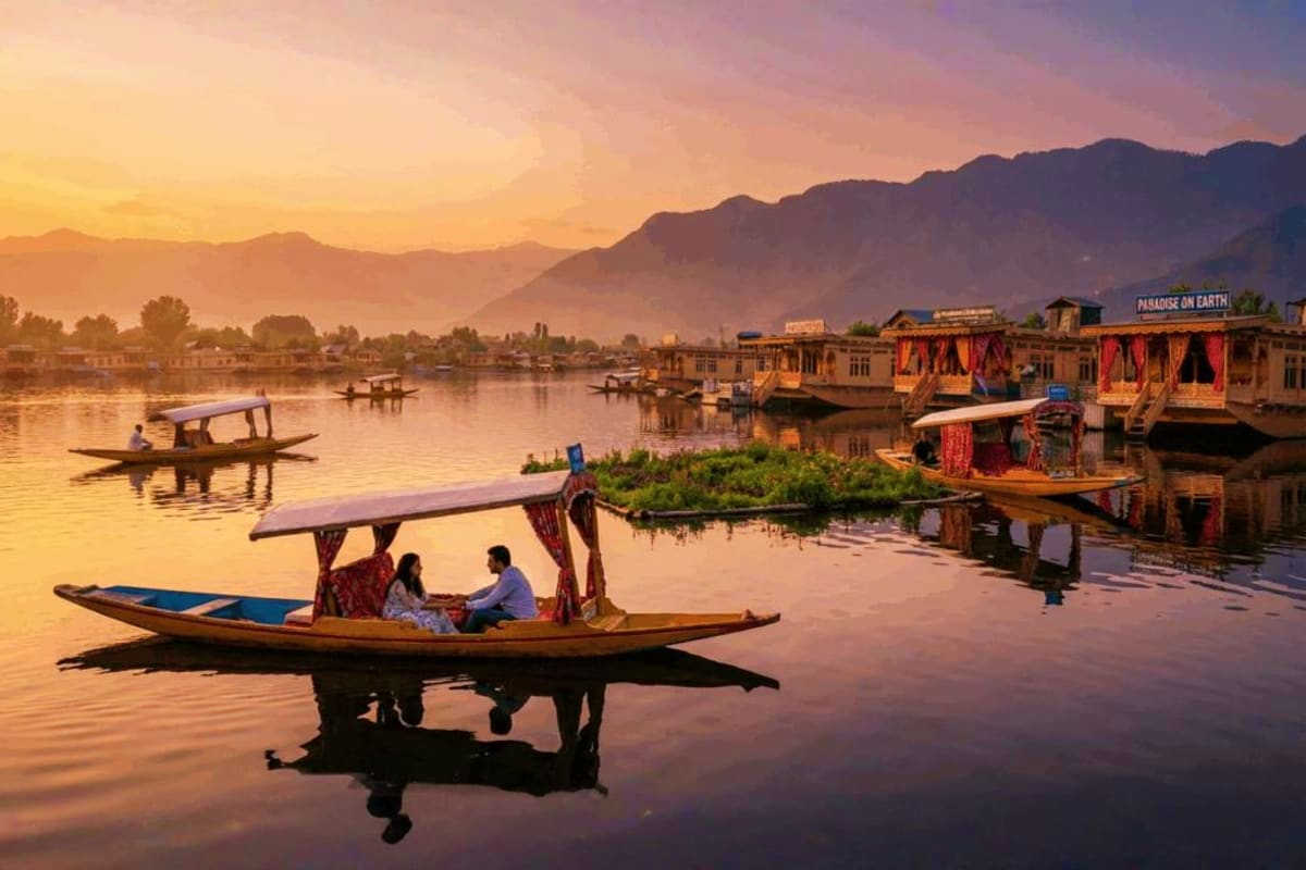 Couple in traditional wooden shikara boat on Dal Lake at sunrise with colorful houseboats and snow-capped mountains in backgr