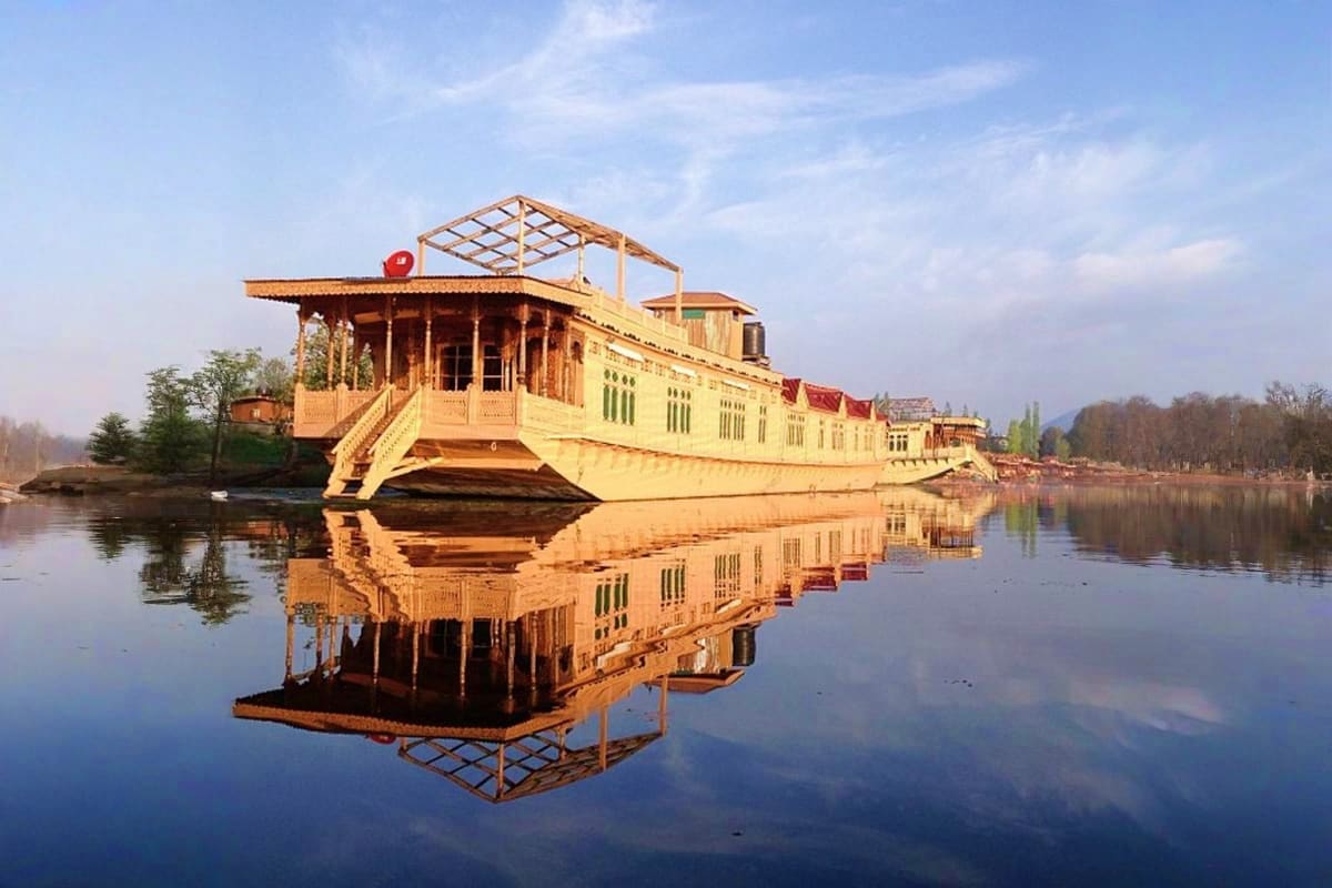 Yellow houseboat with red roof floating on calm water with perfect mirror reflection and mountains in background, Dal Lake Ka